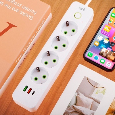 Extensão eléctrica branca com quatro tomadas e três portas USB, ao lado um livro e um smartphone numa mesa de madeira