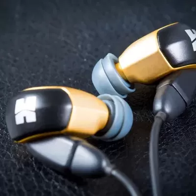 Auriculares dourados e pretos com ponteiras azuis sobre superfície preta