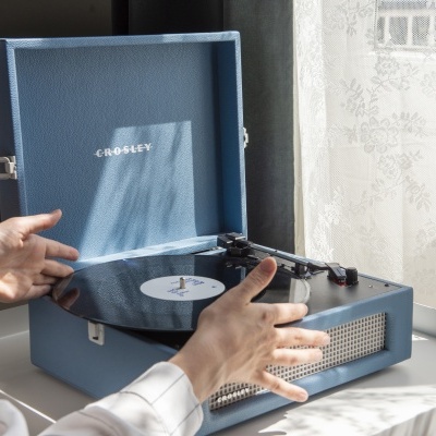 Toca-discos portátil azul CROSLEY aberto junto a janela com cortina branca