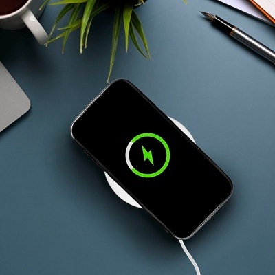 Telefone a carregar sem fios sobre base branca em mesa azul com caneta e planta