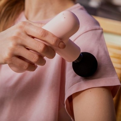 Pessoa a usar massageador portátil rosa com cabeça preta no braço