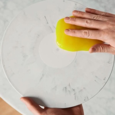 Mão a segurar massa amarela viscosa sobre prato branco com padrão de mármore.