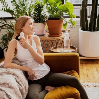 Mulher num sofá com dispositivo no pescoço e plantas ao fundo