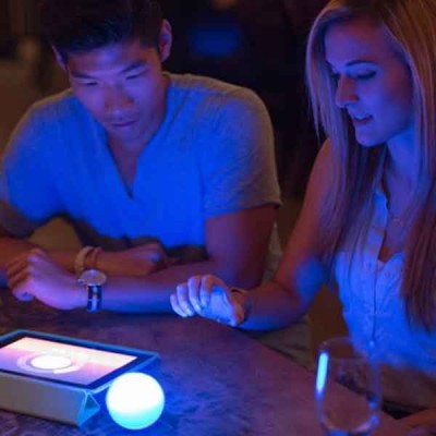 Mesa com tablet branco e esfera luminosa azul com duas pessoas no ambiente azul