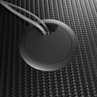 Tampa redonda preta para passagem de cabos numa superfície de fibra de carbono com dois cabos a sair