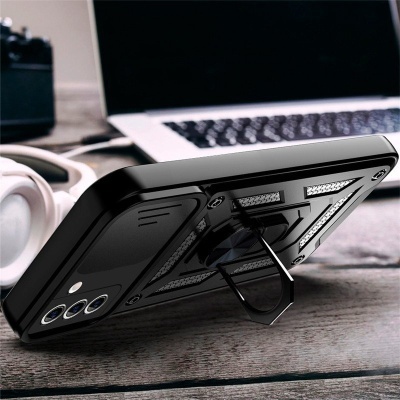 Capa de telemóvel preta com suporte de anel sobre mesa de madeira, auscultadores e portátil ao fundo