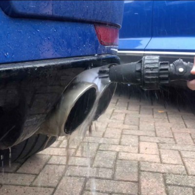 Ponta de escape de carro azul a ser limpa com pistola de alta pressão sobre pavimento cinzento