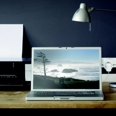 Mesa com impressora, portátil aberto com imagem de mar e candeeiro metálico