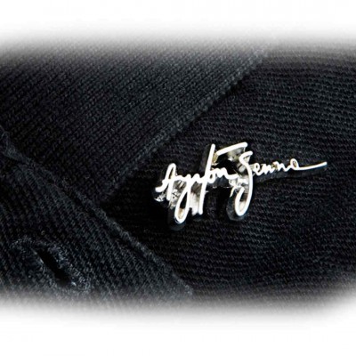 Alfinete prateado com assinatura 'Agatha Segura' em tecido de malha preta