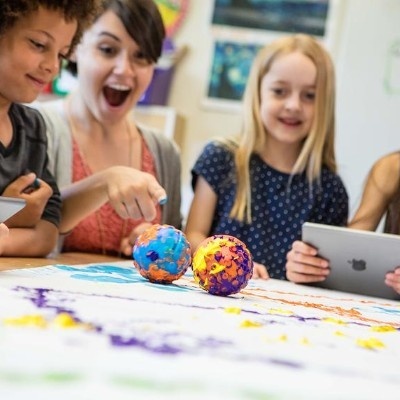 Crianças com tablets e bolas coloridas numa mesa com papel de desenho