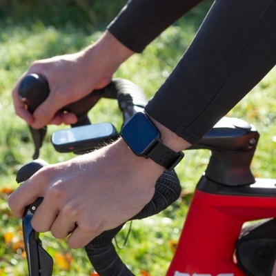 Relógio inteligente preto num pulso segurando o guiador de bicicleta vermelha