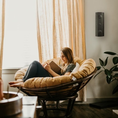 Cadeira redonda com almofada bege e mulher a ler livro junto a janela com cortinas