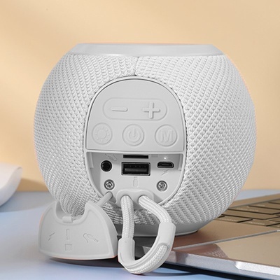 Coluna de som portátil branca com botões e portas visíveis sobre mesa perto de computador portátil