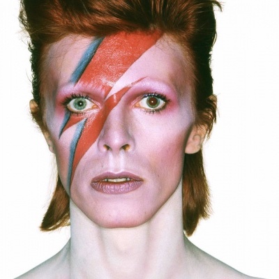 Pessoa com maquiagem em padrão de raio vermelho e azul no rosto e cabelo ruivo