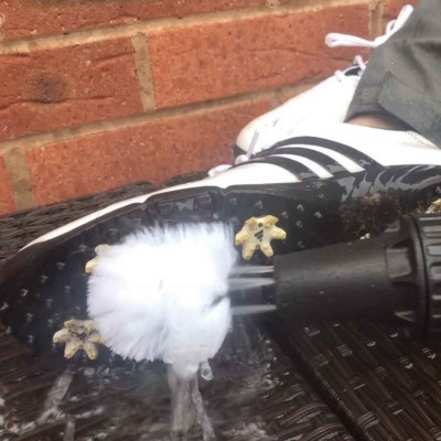 bota desportiva branca com riscas pretas e cravos amarelos a ser limpa com escova molhada