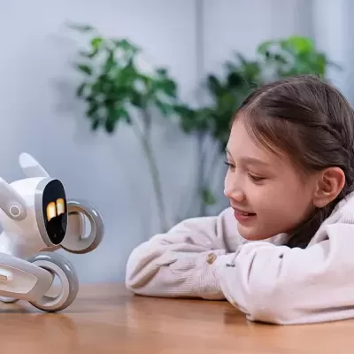 Robot branco com ecrã preto iluminado ao lado de menina sorridente junto a mesa de madeira