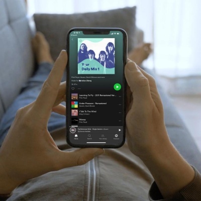 Pessoa a segurar smartphone com playlist Your Daily Mix 1 no Spotify, fundo de sofá e pernas desfocadas