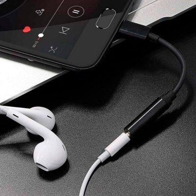 Smartphone preto ligado a auriculares brancos via adaptador preto numa superfície preta