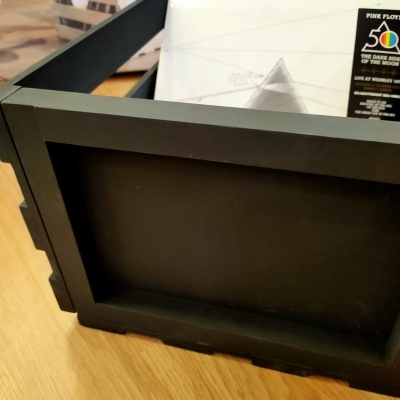 Caixa preta com discos de vinil visíveis, incluindo disco Pink Floyd, sobre chão de madeira