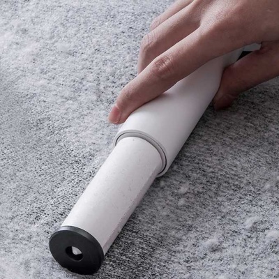 Rolo de massagem manual branco e preto com eixo de madeira segurado por mão sobre superfície cinza.