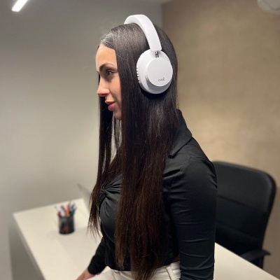 Mulher com auscultadores brancos over-ear sentada numa cadeira junto a secretária branca