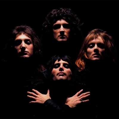 Quatro homens com roupas pretas em fundo escuro, posando com mãos cruzadas no peito.