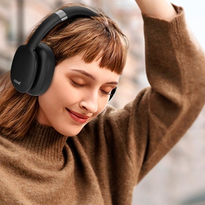 Mulher com headphones pretos de grandes dimensões e casaco castanho num ambiente urbano.