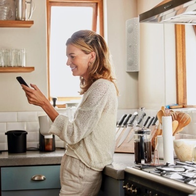 Mulher com camisola bege segurando smartphone numa cozinha moderna
