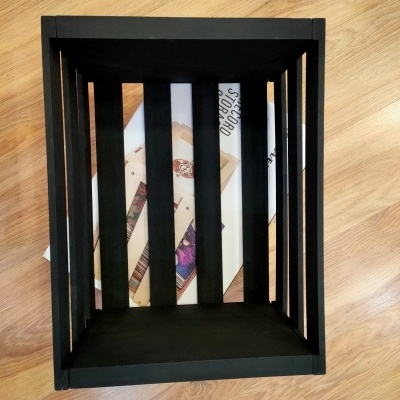 Caixa de madeira preta retangular sobre chão de madeira clara com livros dentro