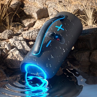 Coluna Bluetooth portátil preta com botões azuis e LED azul em ambiente exterior