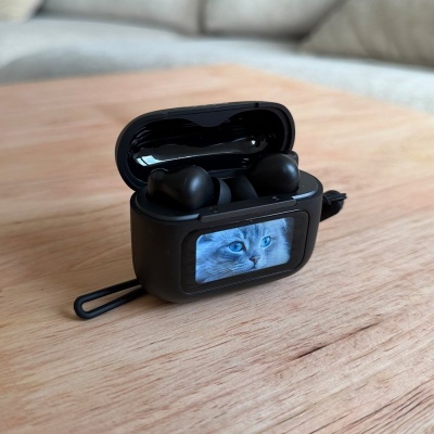 Auriculares sem fios num estojo preto aberto com imagem de gato num ecrã