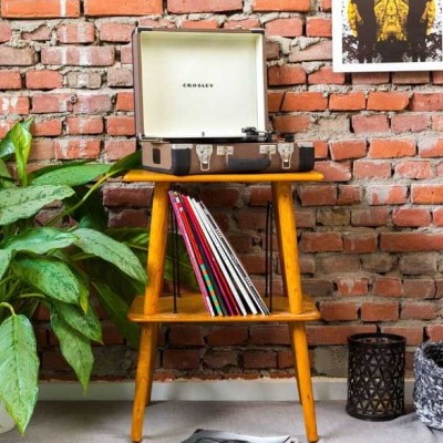 Mesa de madeira com gira-discos CROSLEY, discos de vinil, planta verde e parede de tijolos