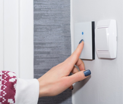 Mão feminina a pressionar interruptor de luz branco com botão azul na parede