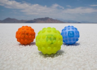 Três bolas coloridas texturizadas sobre superfície branca com montanhas ao fundo