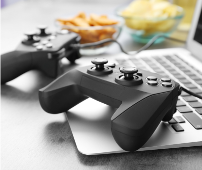 Dois comandos de jogo pretos sobre portátil com tigelas de snacks ao fundo.