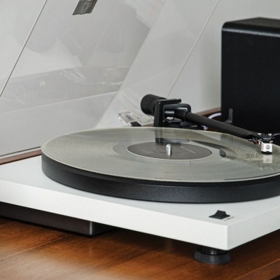 Toca-discos branco com prato transparente e braço preto numa superfície de madeira