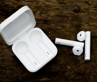 Fones de ouvido sem fios brancos com estojo de carregamento aberto sobre madeira