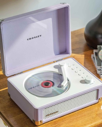 Leitor de vinil lilás claro aberto com prato branco e botões numa mesa de madeira