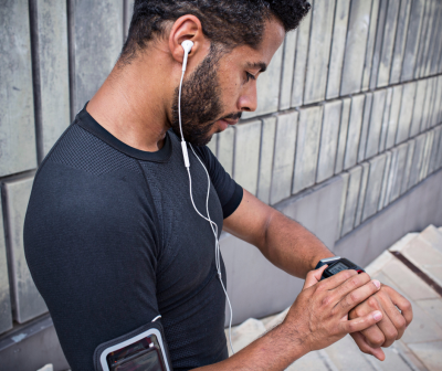 Homem com roupa desportiva e auriculares usando smartwatch e telemóvel numa braçadeira junto a parede