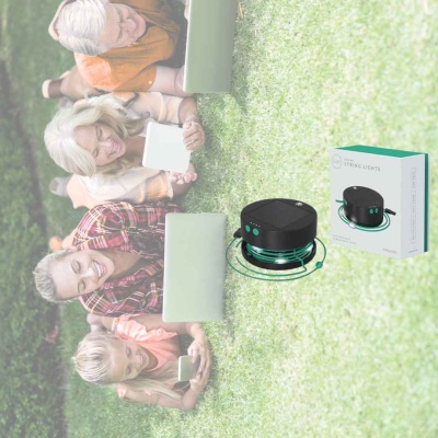 Grupo de pessoas na relva com dispositivos digitais e um dispositivo preto redondo com caixa ao lado.