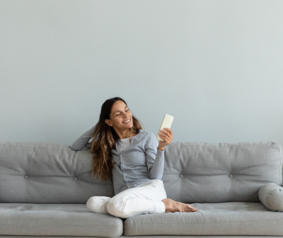 Mulher sentada num sofá cinzento claro a sorrir e segurando uma embalagem branca