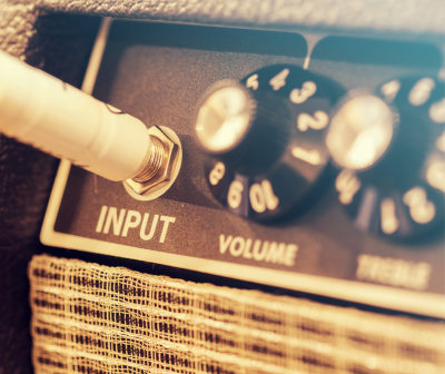 Amplificador preto com entrada de cabo branco e botões de volume e treble