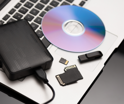 Disco CD/DVD, disco rígido externo, cartões de memória SD e pen USB sobre laptop