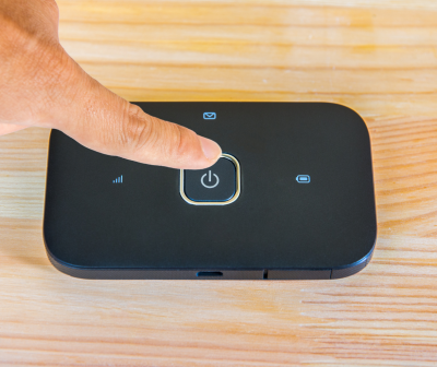 Modem portátil preto com ícones LED numa superfície de madeira clara.