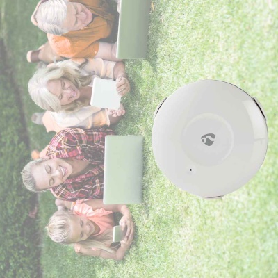 Robô aspirador branco redondo numa relva verde com quatro pessoas deitadas atrás dele