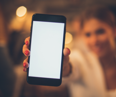 Smartphone com ecrã branco segurado na mão de uma pessoa com unhas vermelhas