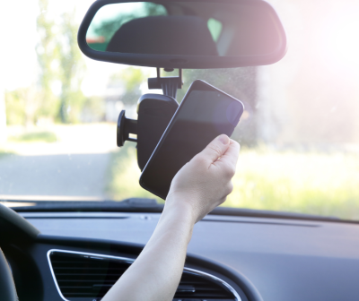 Suporte de telemóvel preto no para-brisas de um carro com mão a colocar telemóvel