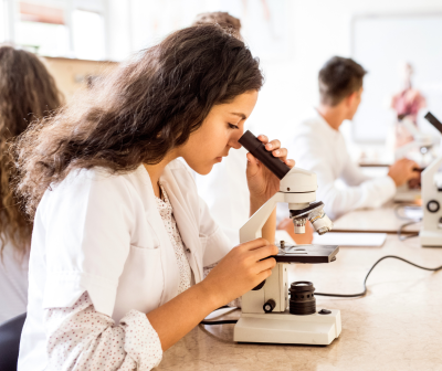 Mulher em bata branca a usar microscópio num laboratório