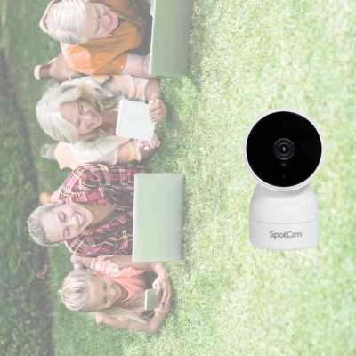 Câmera SpotCam branca posicionada na relva com quatro pessoas deitadas ao fundo