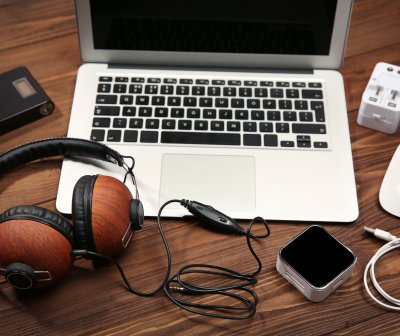 Notebook prateado, auscultadores de madeira e acessórios eletrónicos sobre mesa de madeira